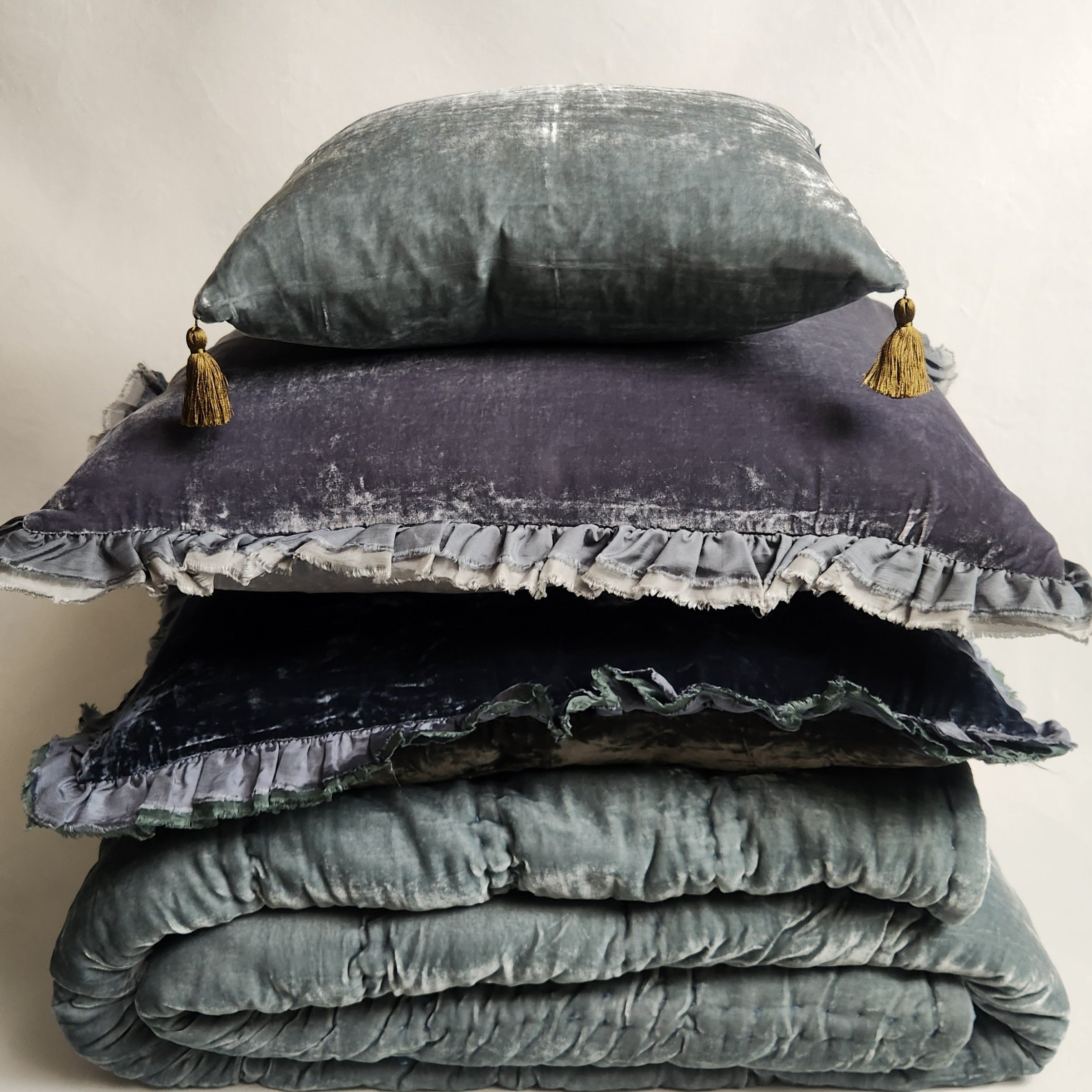 Stack of textured blue /green bedding with a matching pillow on a neutral background