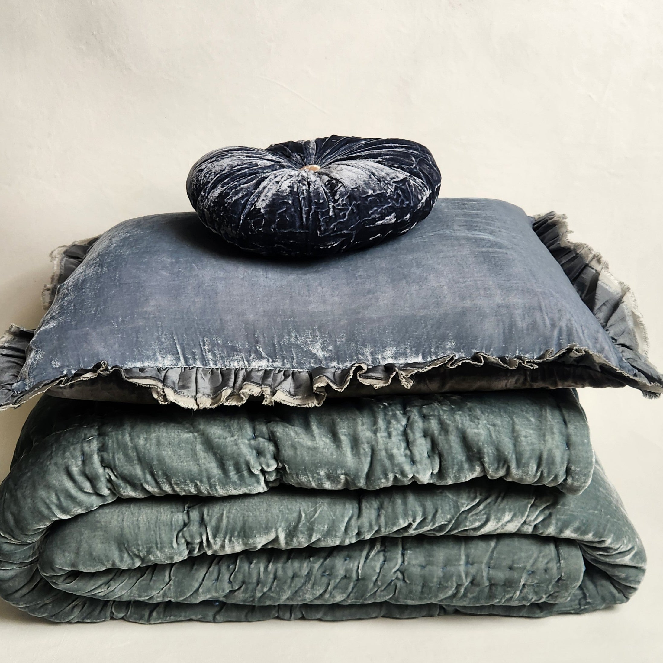 Stack of textured blue /green bedding with a matching pillow on a neutral background
