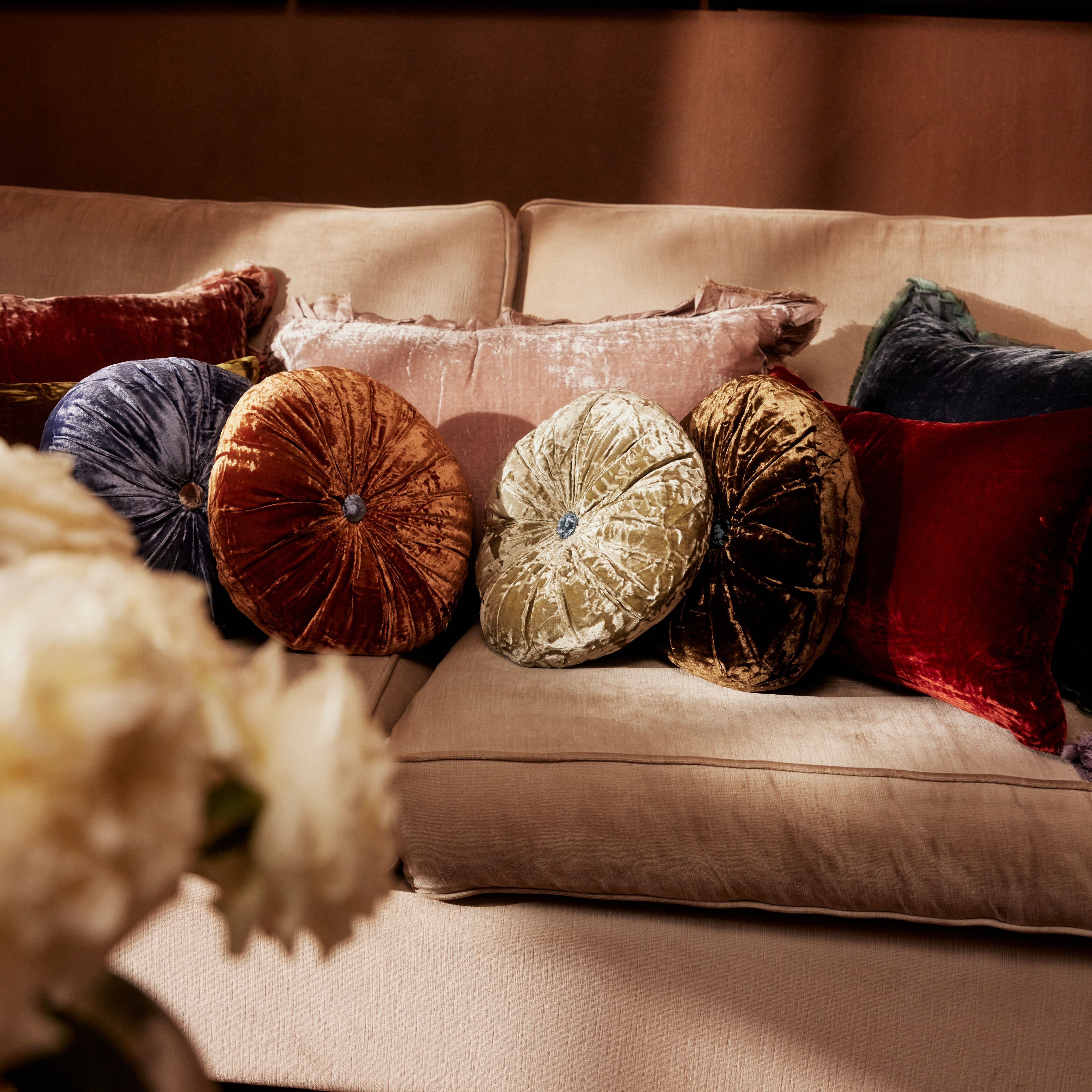 A green round silk velvet cushion with a contrasting button, displayed with other cushions.