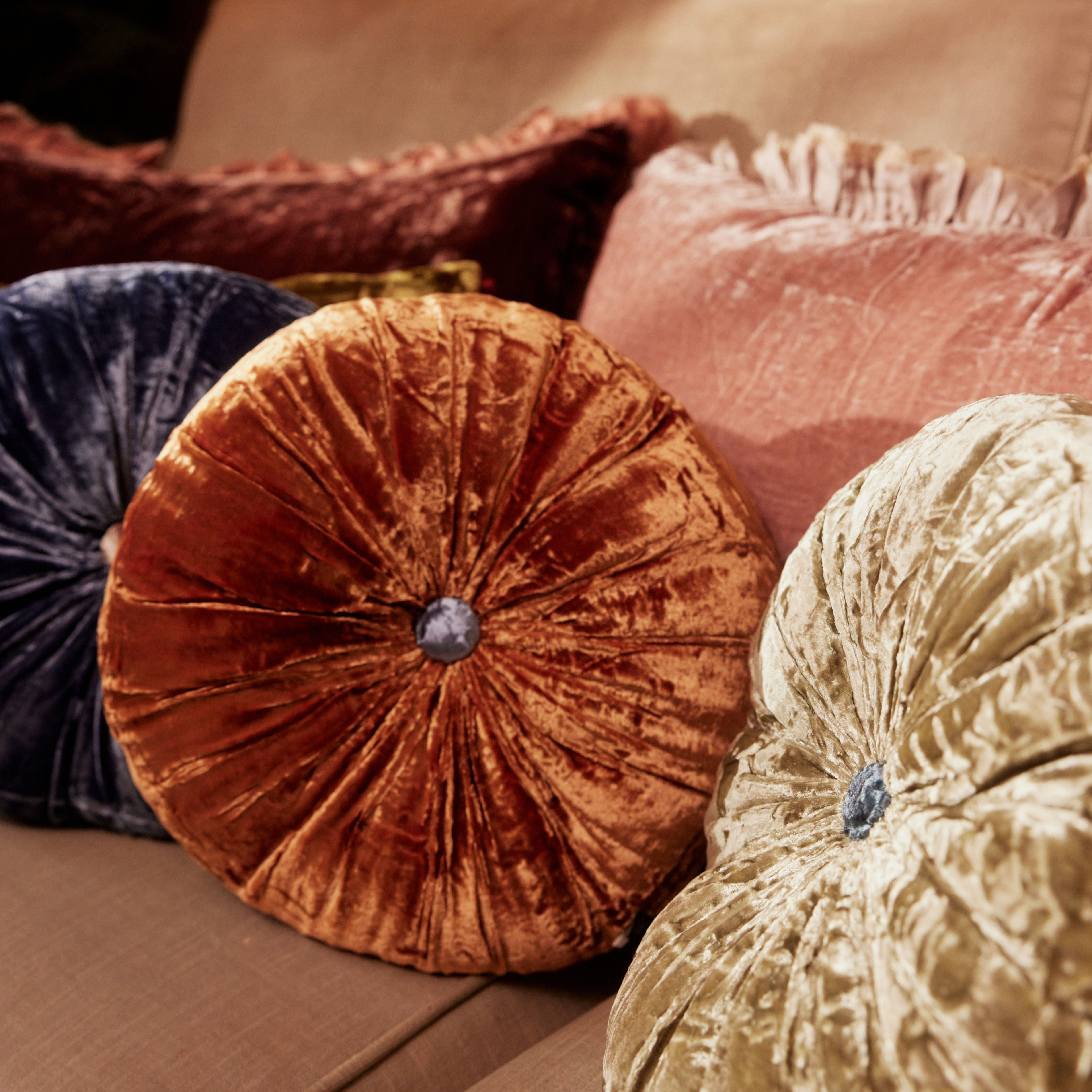 A round silk velvet cushion in Bombay orange with a contrasting button, displayed with other cushions.