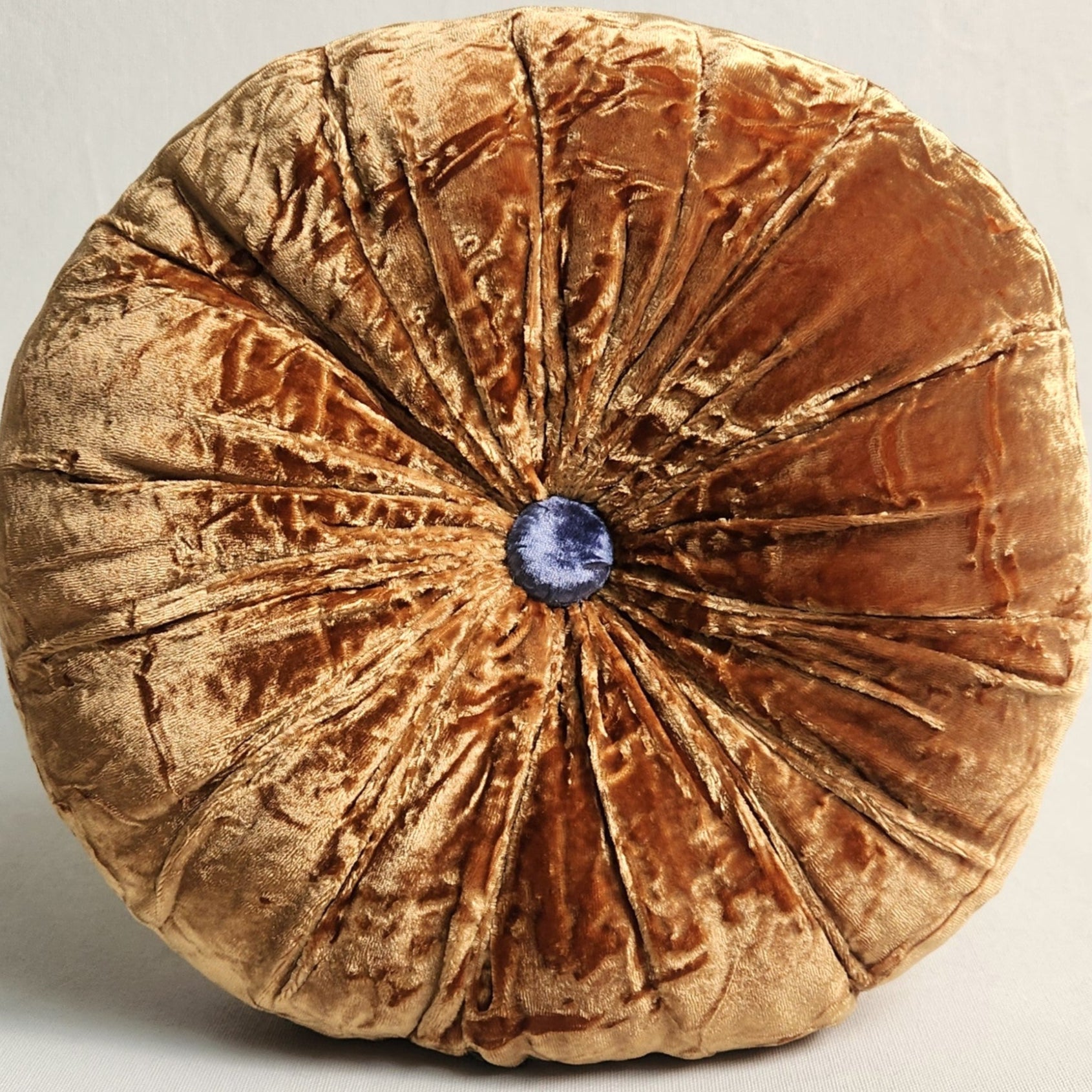 A round silk velvet cushion in Bombay orange with a contrasting button.