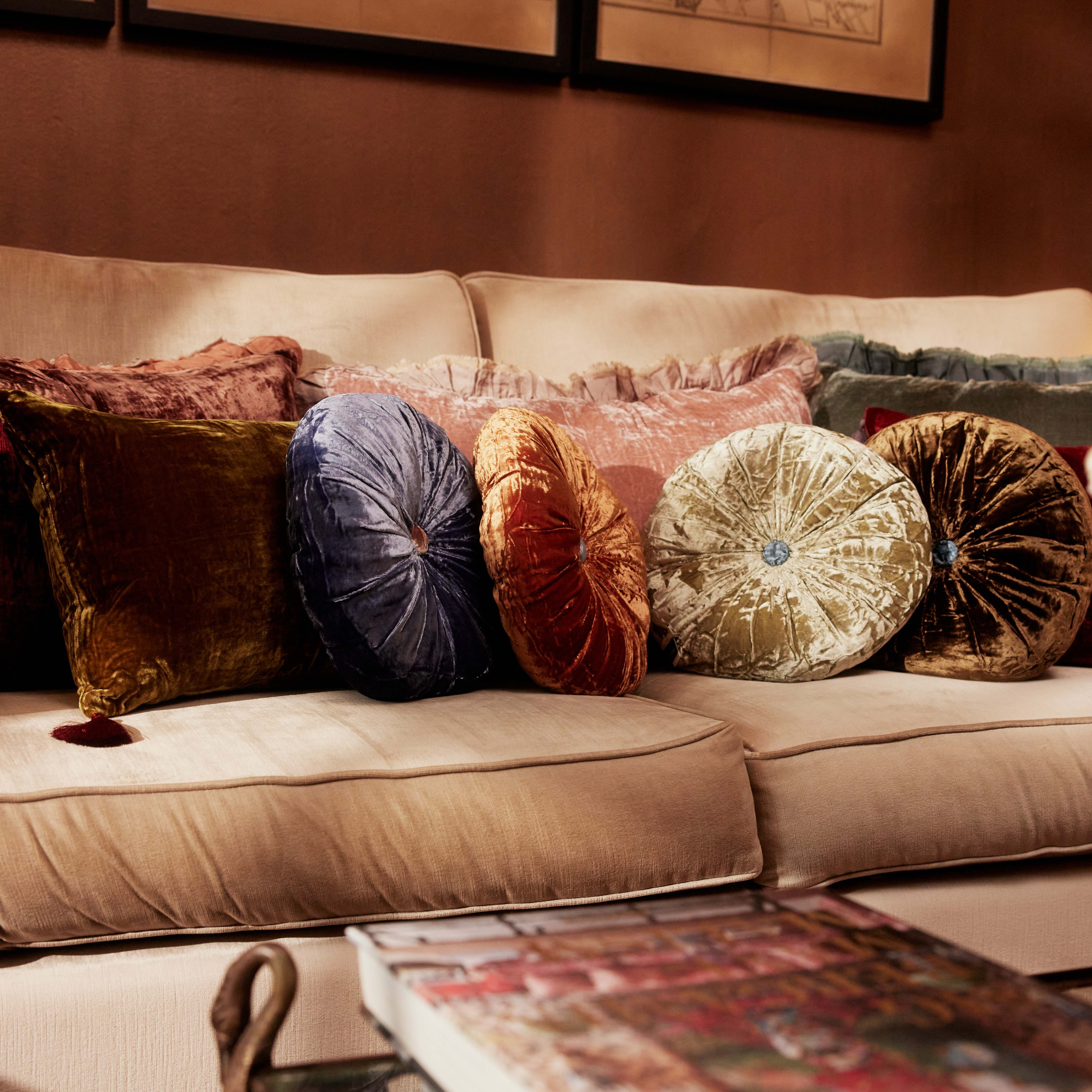 A round silk velvet cushion in delft blue with a contrasting button, displayed with other silk velvet cushions.