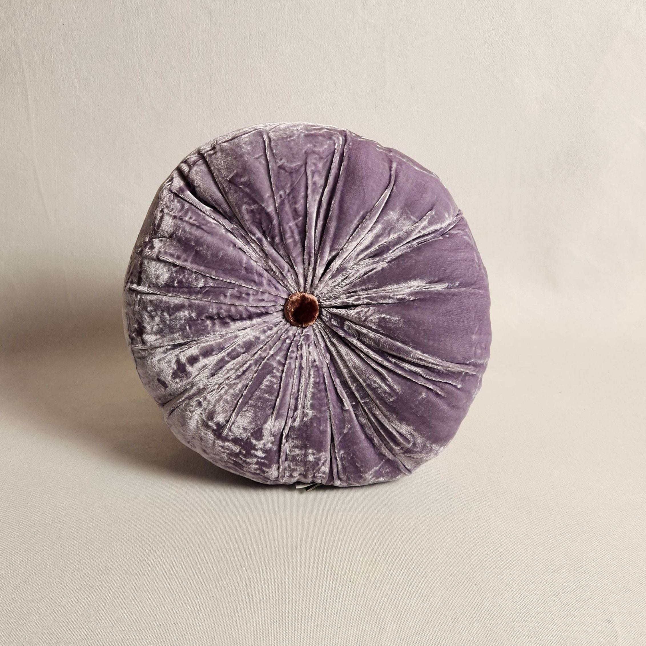Round purple velvet pillow on a beige background