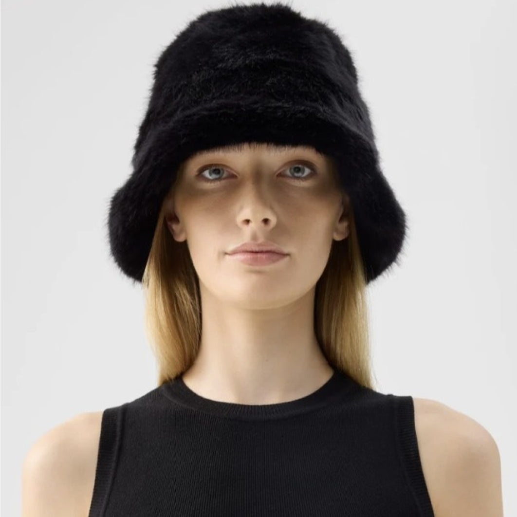 A woman wearing a black fuzzy bucket hat and a black ribbed sleeveless top, photographed against a light gray studio background.