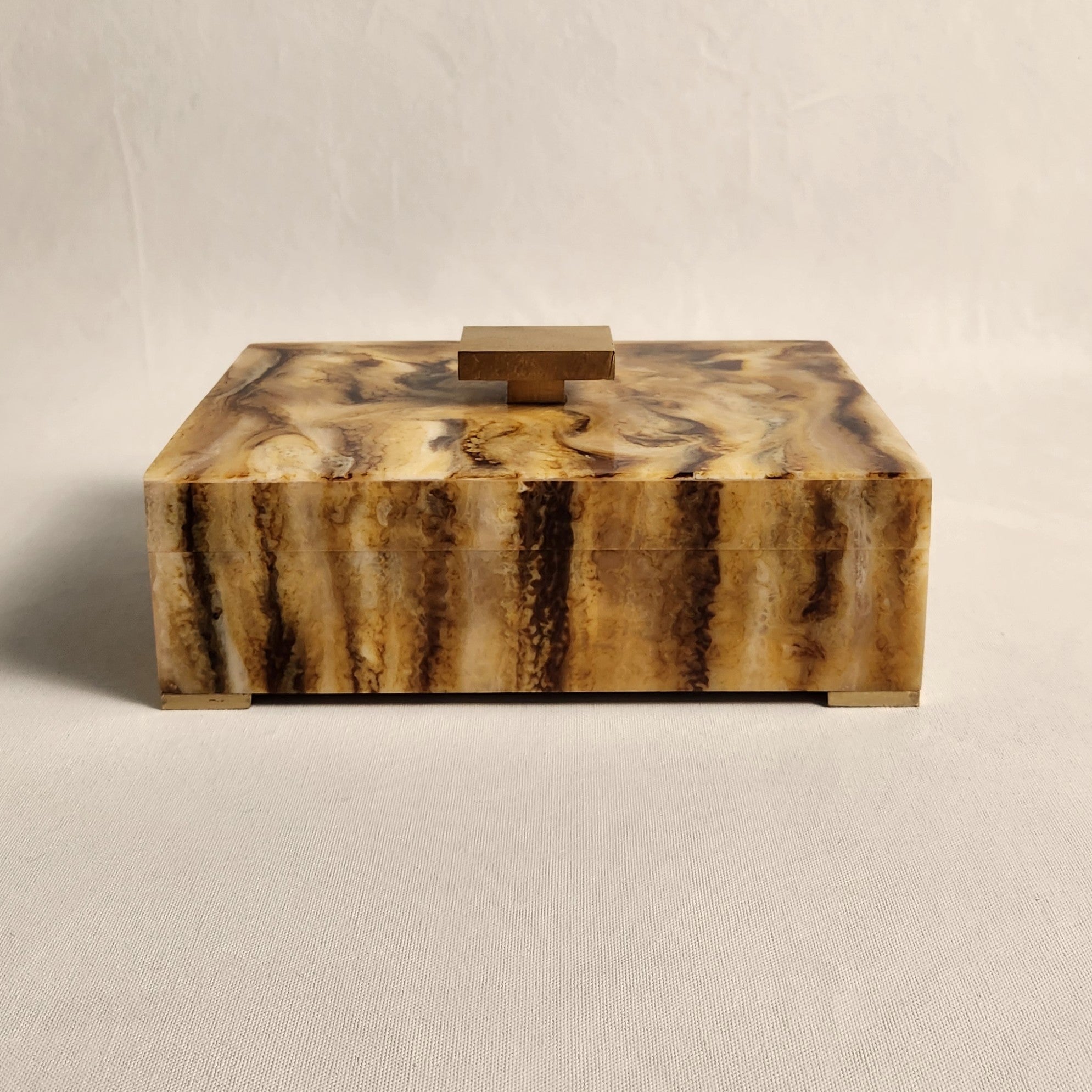 Marbled toffee and gold jewelry box with a gold handle on a beige background