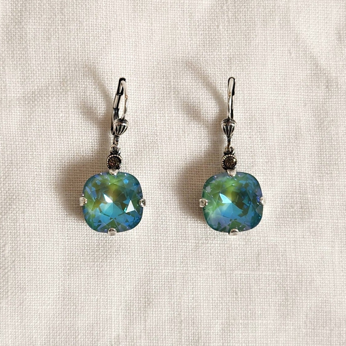 Pair of earrings with blue and green gemstones on a beige fabric background