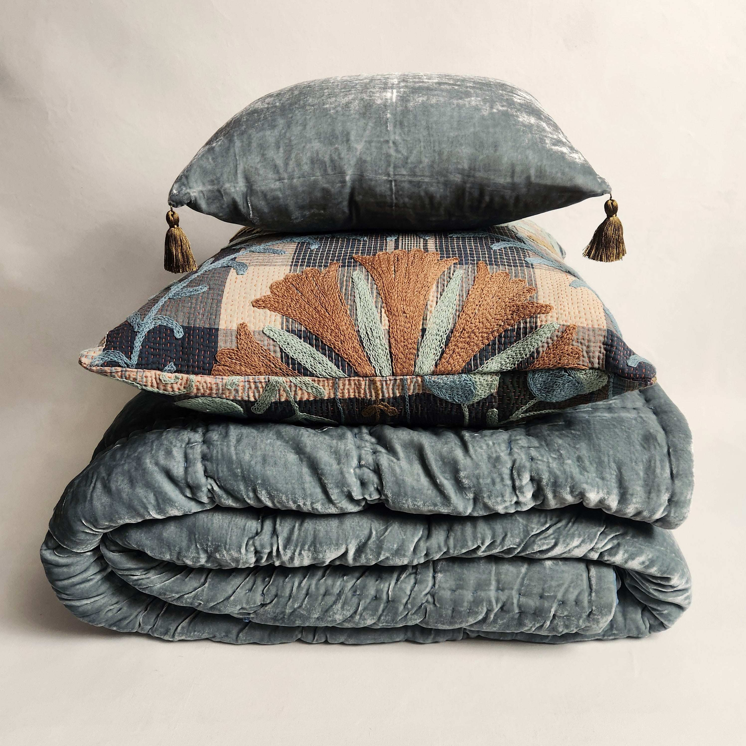 Stack of textured blue bedding with a patterned pillow on a neutral background