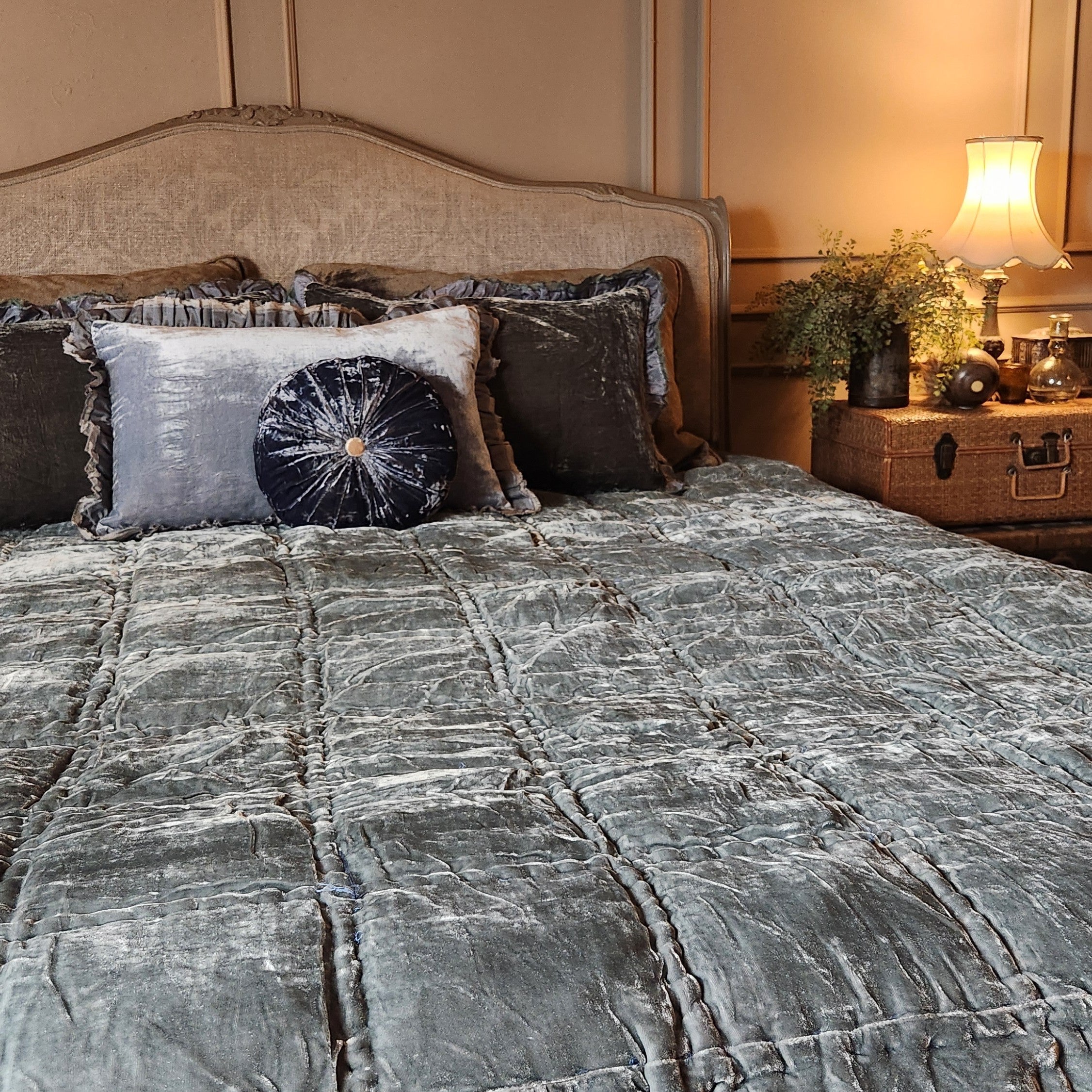 Bed with silk velvet bedding and decorative pillows in a bedroom setting.
