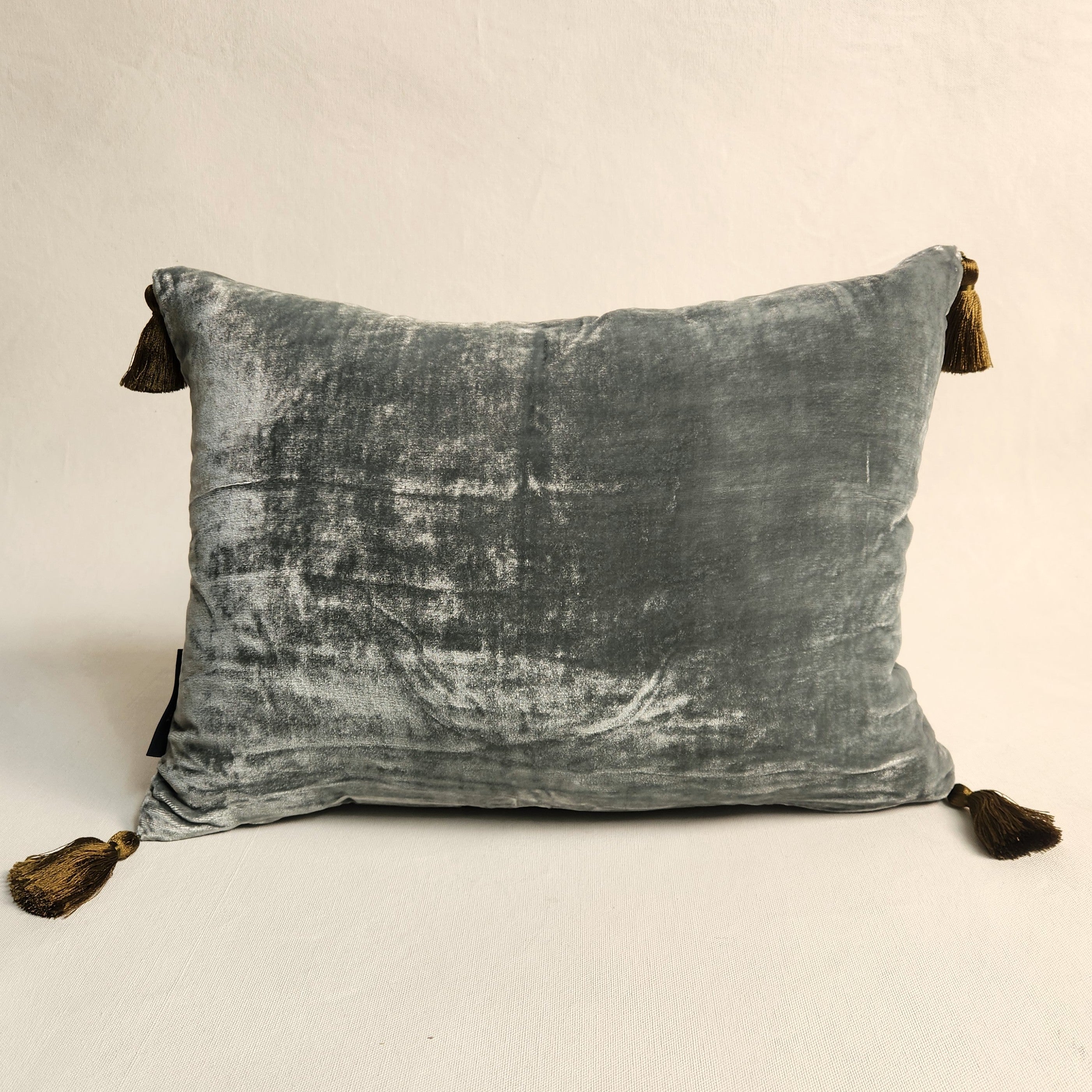 Blue green silk velvet pillow with contrasting tassels .