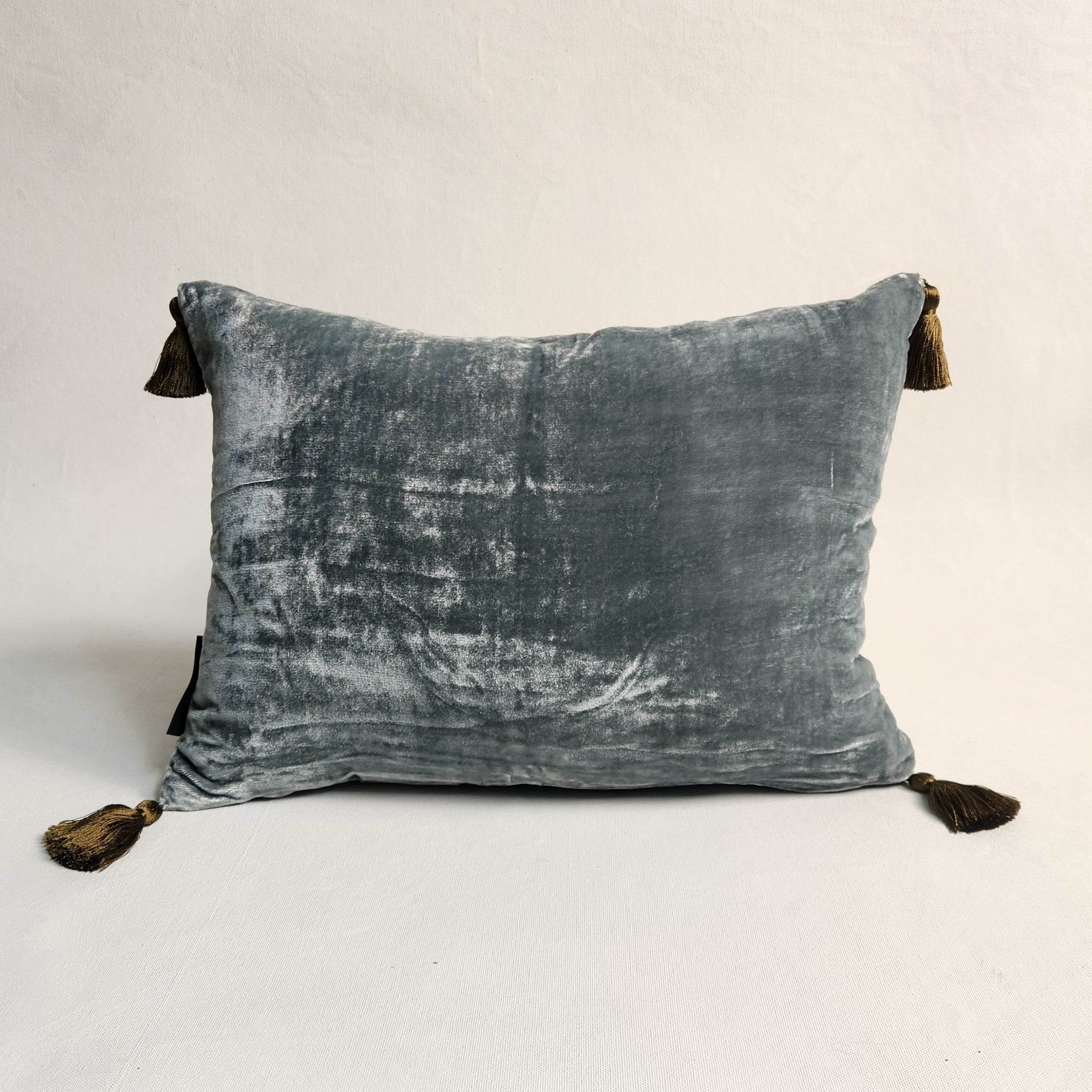 Blue green silk velvet pillow with tassels on a neutral background