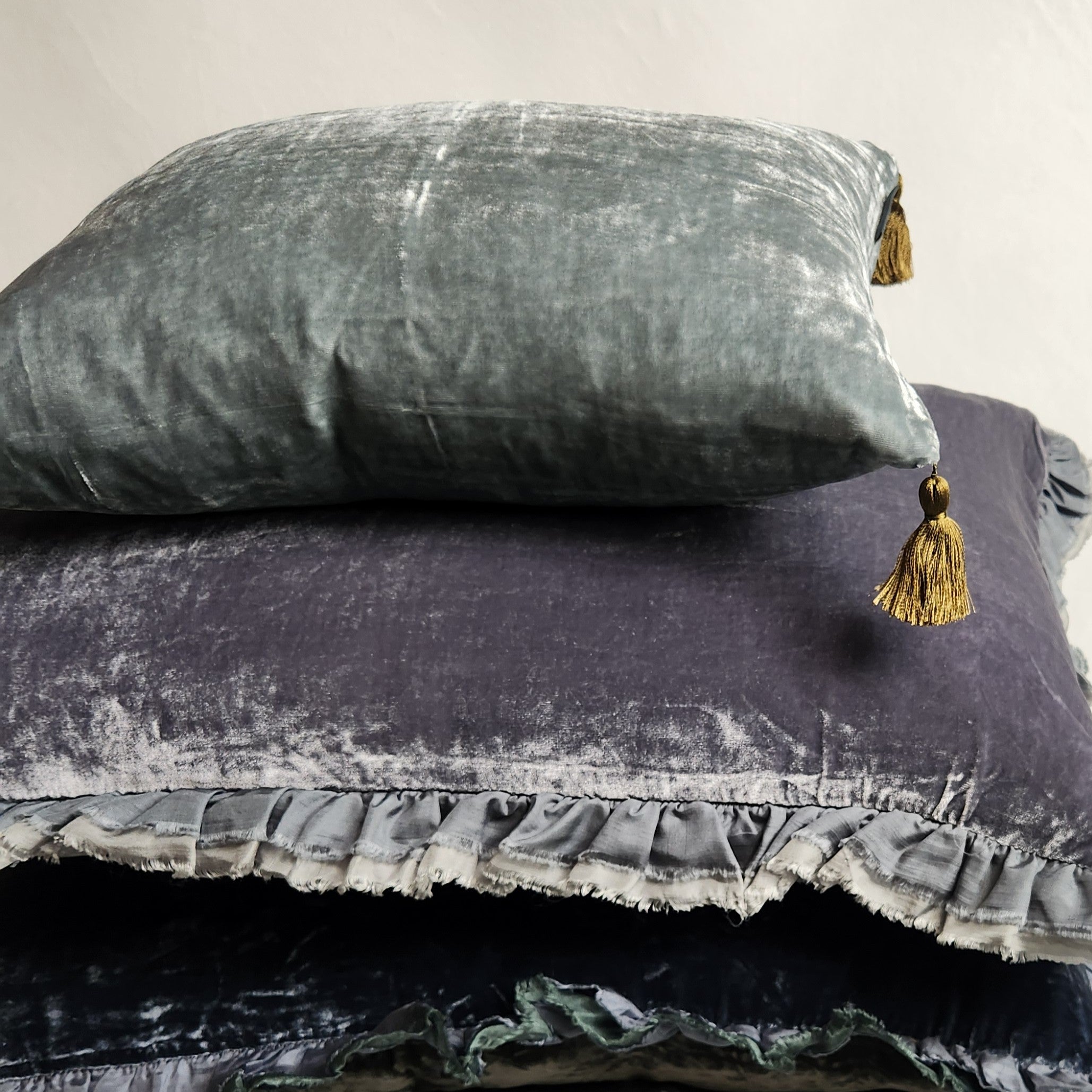 Blue green silk velvet pillow with contrasting tassels displayed with other silk velvet cushions.