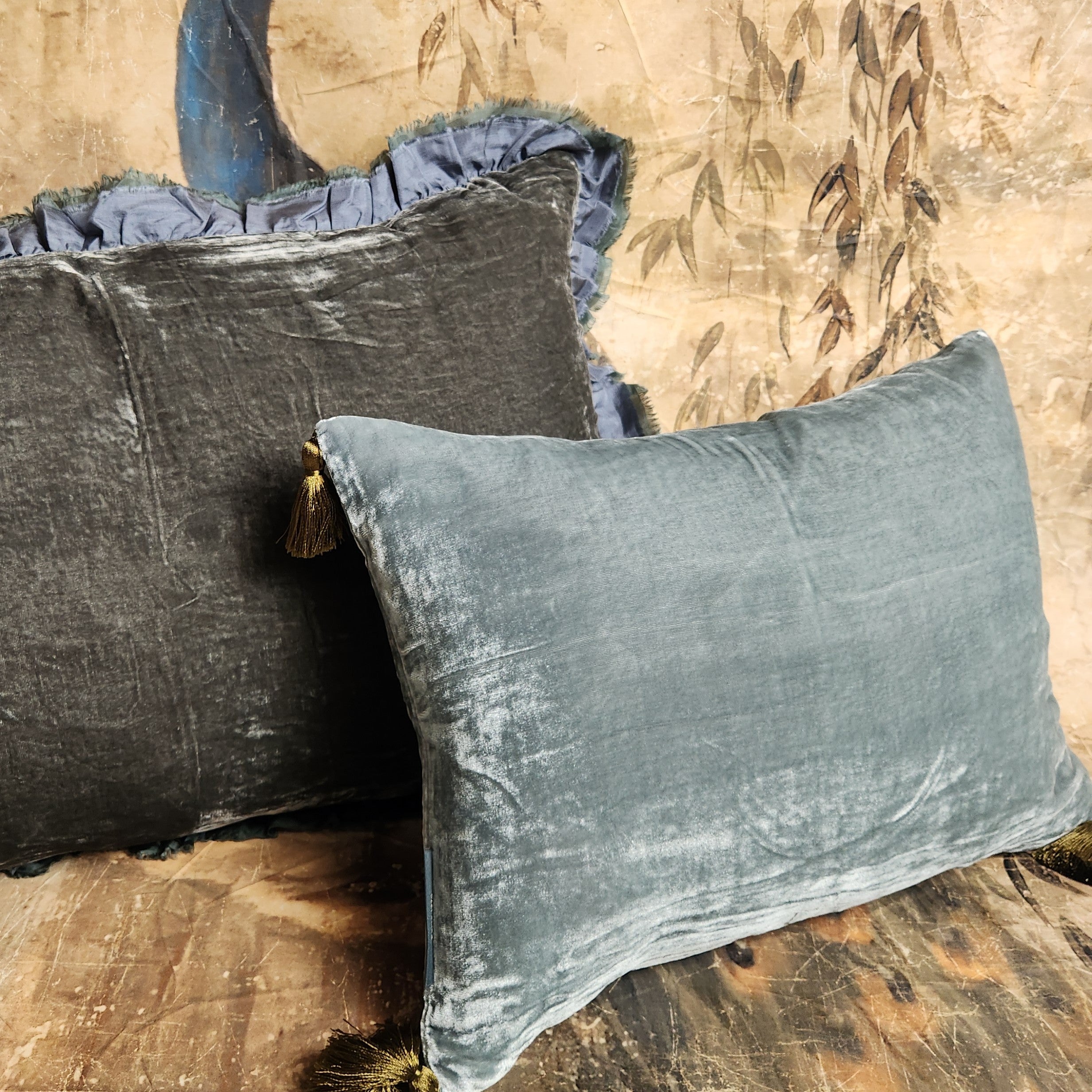Blue green silk velvet pillow with contrasting tassels displayed with other cushions.