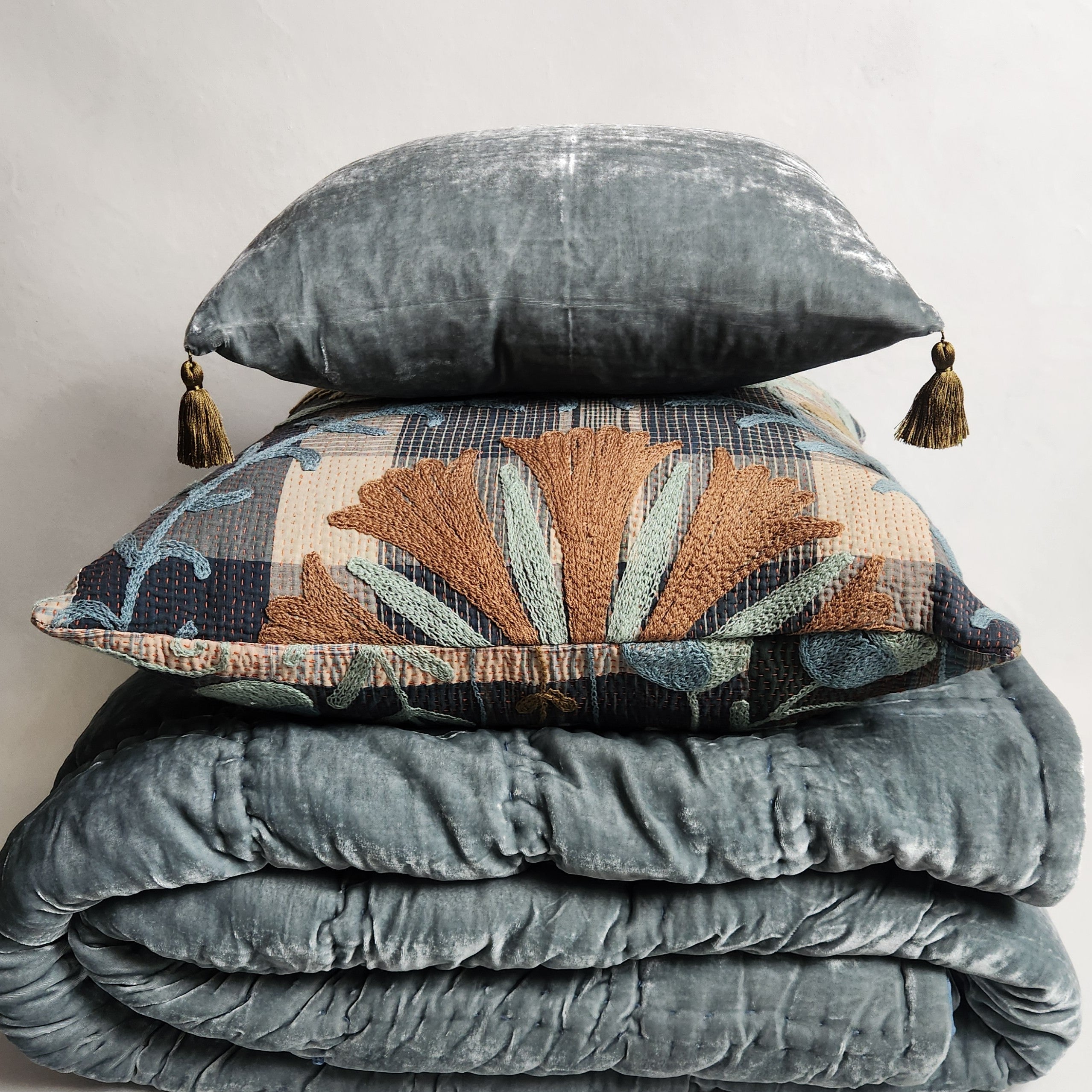 Blue green silk velvet pillow with contrasting tassels displayed with other cushions.