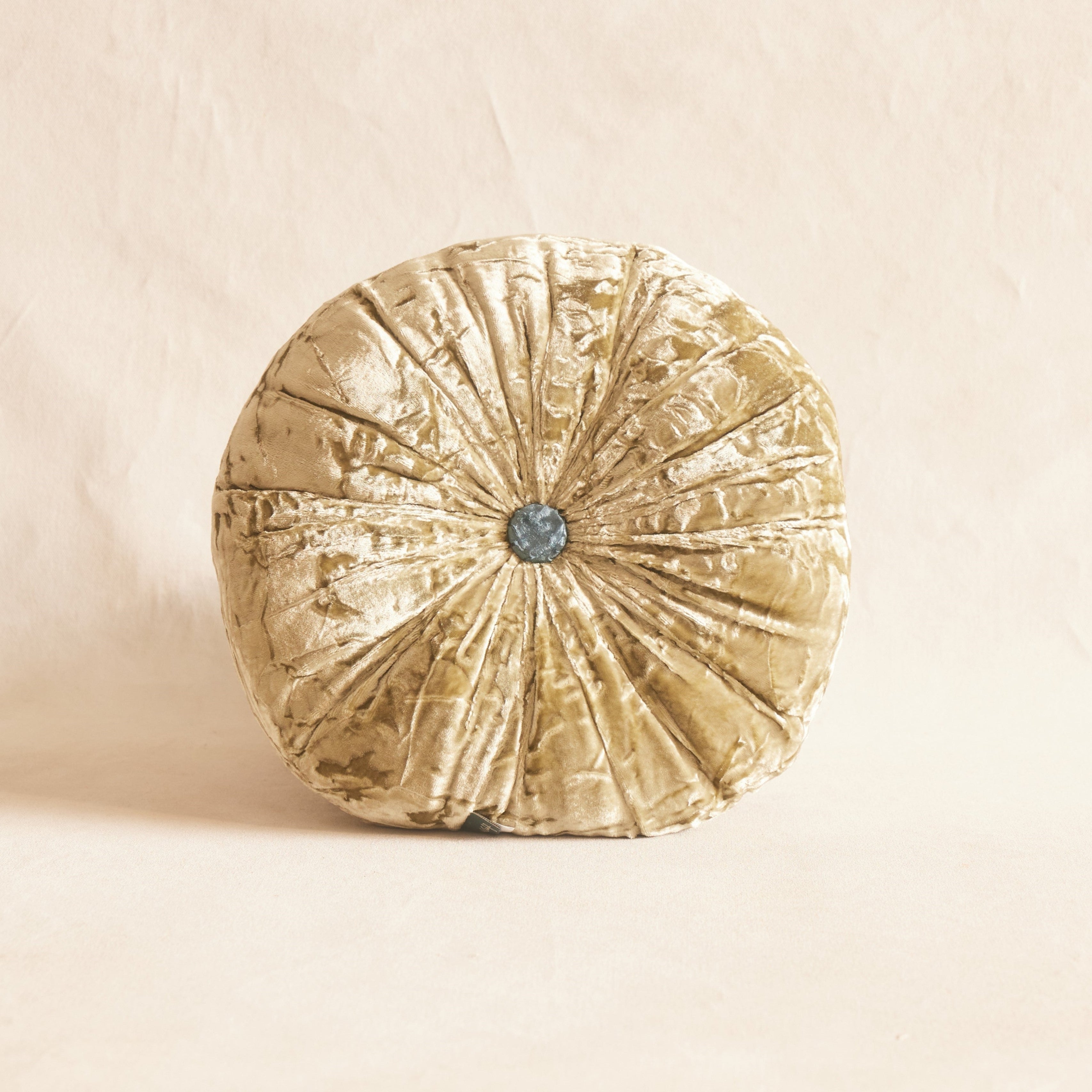 A round, green silk velvet cushion with a decorative button in the center, displayed against a neutral background.