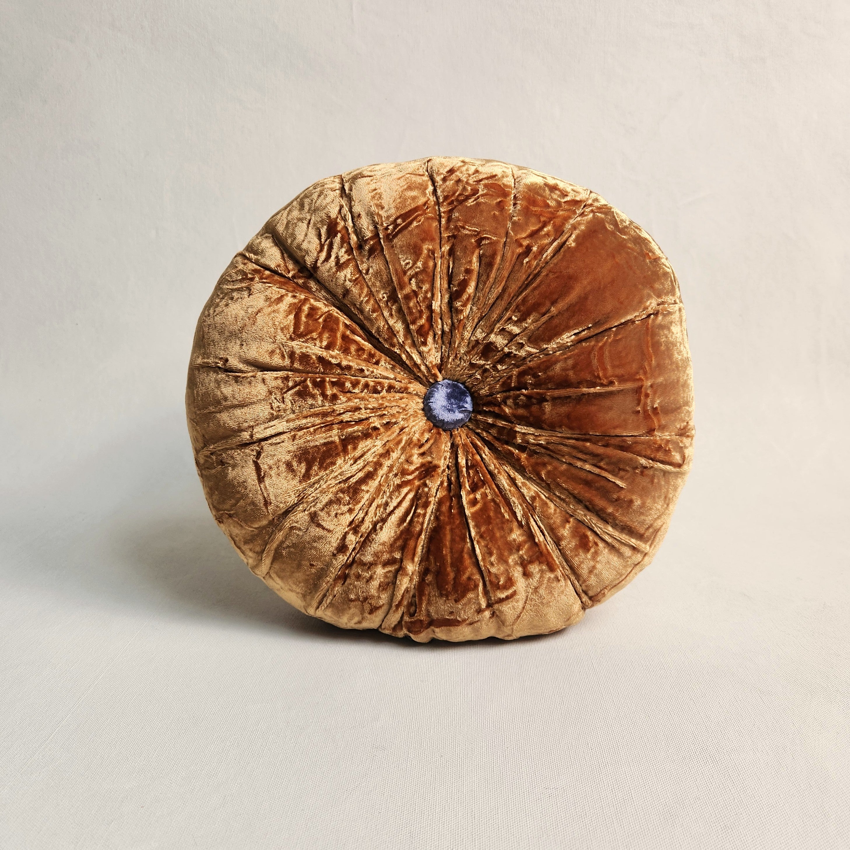 A round silk velvet cushion in Bombay orange with a contrasting button, feather/poly infill.