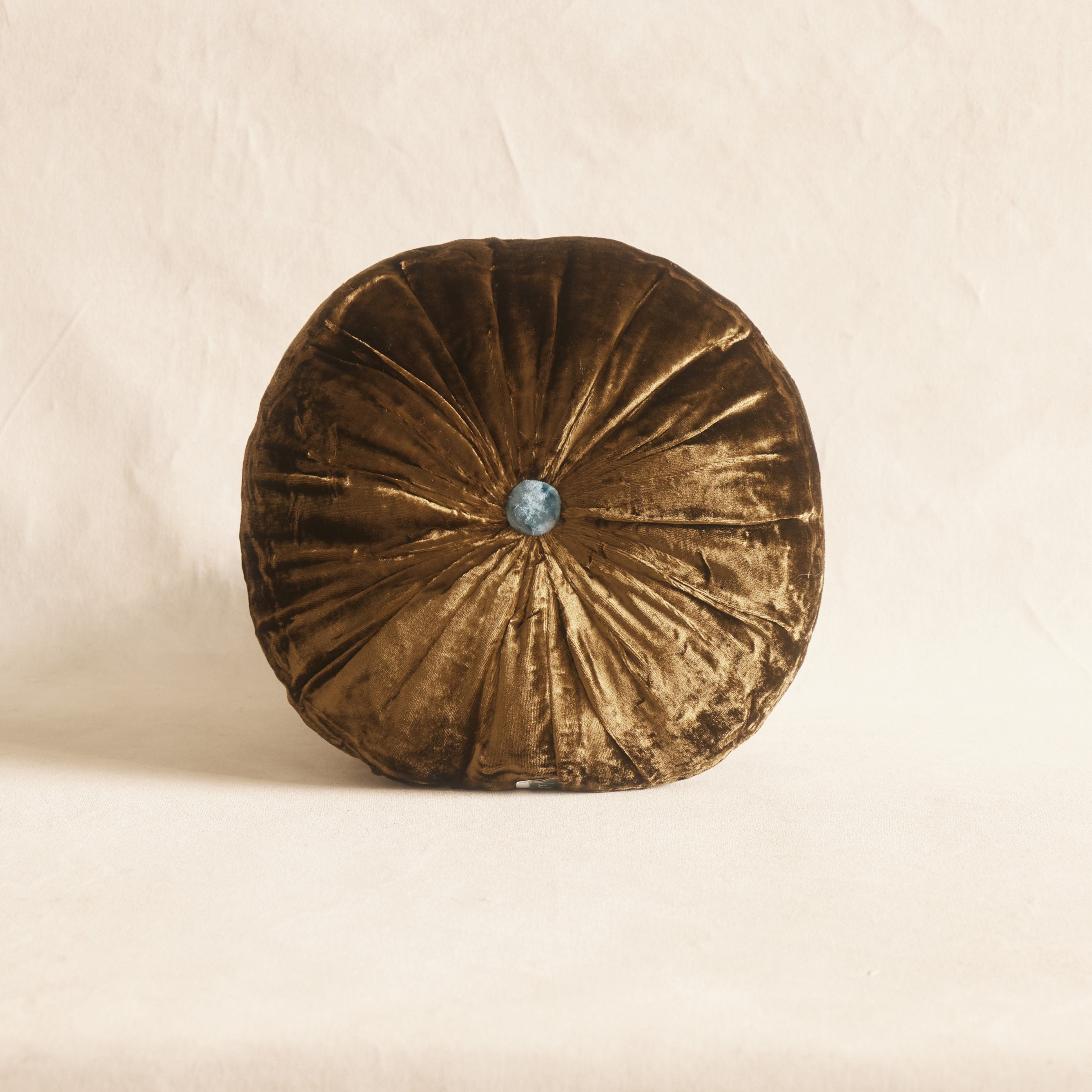 A round silk velvet cushion in brown color with a contrasting button, displayed on a neutral background.