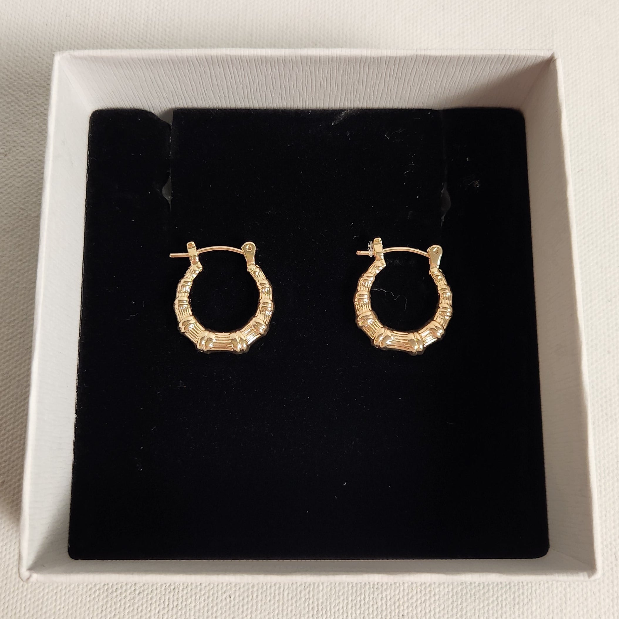 Gold hoop earrings in a black box on a beige surface